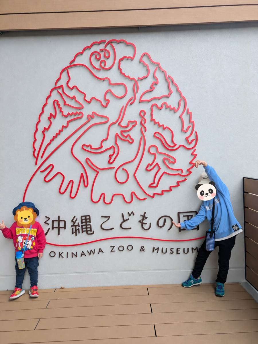沖縄こどもの国の施設看板前に立つ子どもたち。顔はスタンプで保護